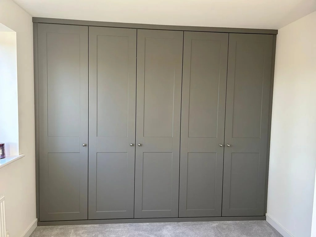 Spacious built-in wardrobe with six matte gray doors and small round handles. The wardrobe is set against a light-colored wall, conveying a minimalistic and modern tone.